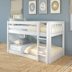 White wooden twin-over-twin bunk bed with ladder and safety rails in a children's bedroom, yellow-striped bedding, blue pillows, moon-and-star wall art and woven jute rug