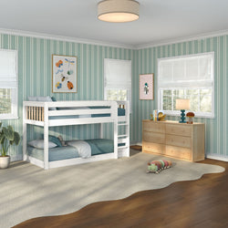 Bright kids bedroom featuring a white wooden bunk bed, teal vertical striped wallpaper, natural wood dresser, plush beige rug, stuffed caterpillar toy, windows with white Roman shades, lamp and framed insect artwork.