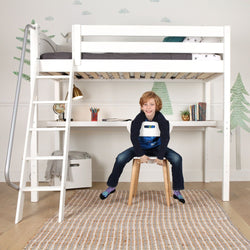 White kids loft bed with desk and ladder, built-in study area under bed with lamp, books and globe, child sitting on stool in children's bedroom
