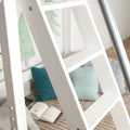 White wooden loft ladder leaning in a cozy bedroom setting with teal throw pillows, woven rug, and an open book