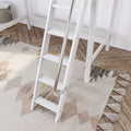 Close-up of a white loft bed ladder with stainless steel handrail on a beige geometric boho rug with tassels, next to herringbone wood flooring and a woven storage basket.