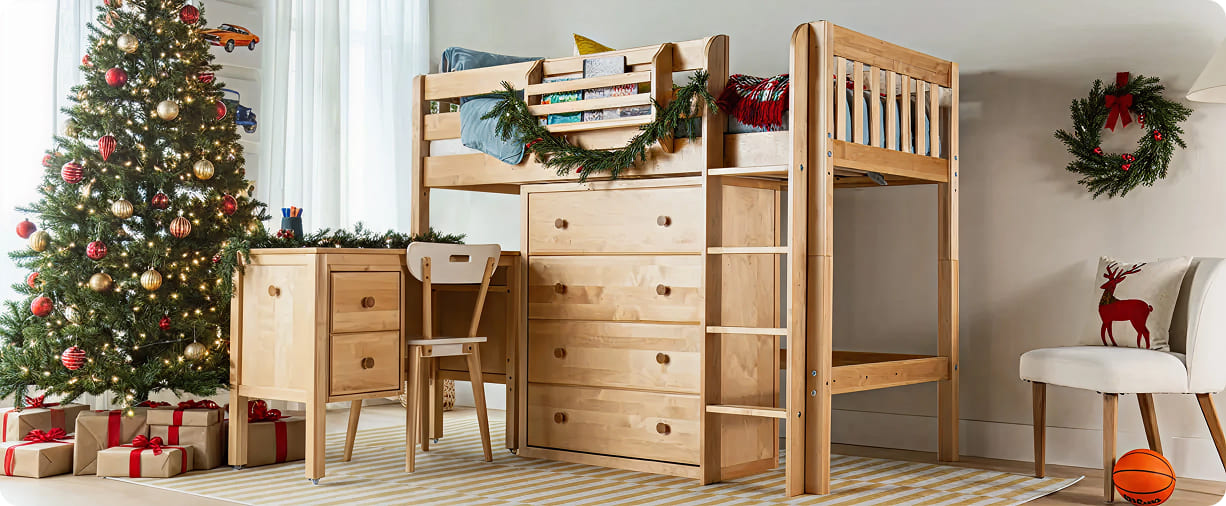 Wooden kids loft bed with built-in drawers and desk in a children's room decorated for Christmas with a lit Christmas tree, wrapped gifts, wreath and festive pillow