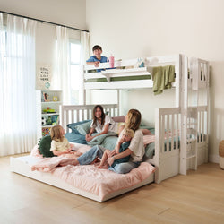 White wooden loft bunk bed with pull-out trundle and kids playing on pastel bedding in a bright modern children's bedroom with bookshelf and sheer curtains
