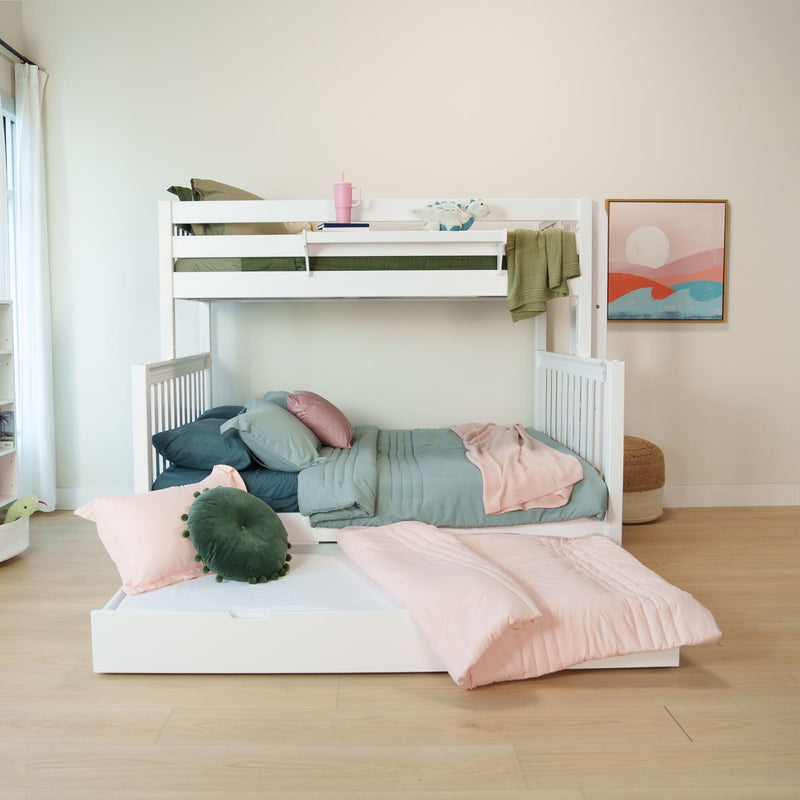 White kids' bunk bed with pastel pink and mint bedding, pull-out trundle, green knit throw, plush dinosaur toy and framed wall art in a bright children's bedroom