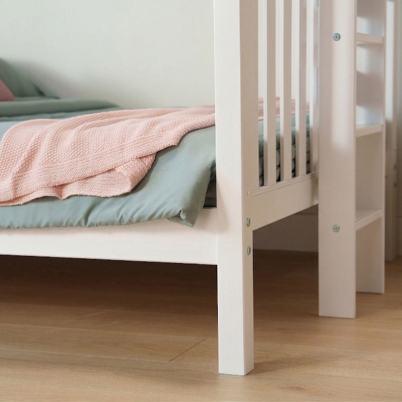 Close-up of a white wooden baby crib with a pink knitted blanket and sage-green bedding on a light hardwood nursery floor