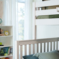 Bright modern nursery with white crib railing, green bedding, toy-filled bookshelf, yellow alarm clock and sheer curtains