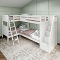 White L-shaped wooden bunk bed with built-in staircase storage and ladder, blush quilts and patterned pillows in a kids' room with sage green paneled walls and textured area rug