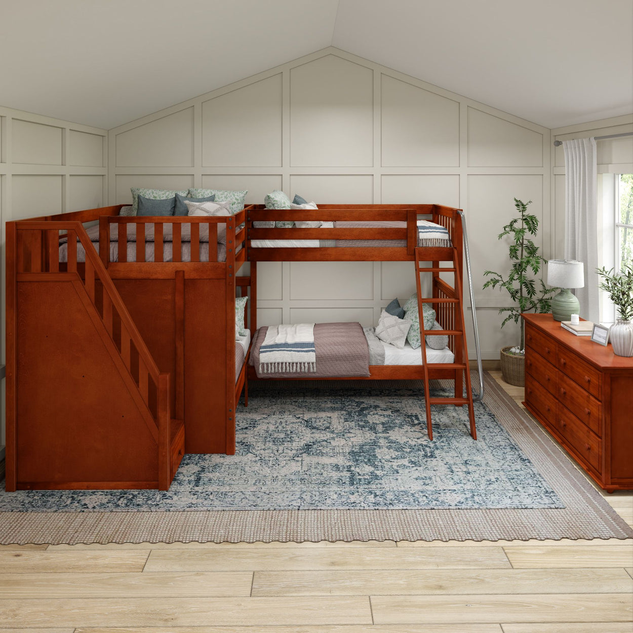 Wooden triple bunk bed with stairs in modern bedroom featuring patterned rug and wooden dressers.