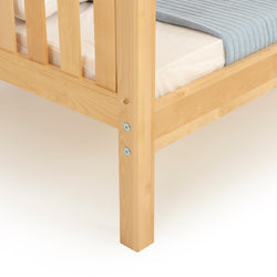 Close-up of light natural solid wood bed frame corner with slatted side rail, sturdy leg and visible metal fasteners, mattress with light blue quilt