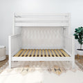 White wooden crib frame with slatted mattress support in a modern minimalist nursery featuring a patterned rug and potted plant