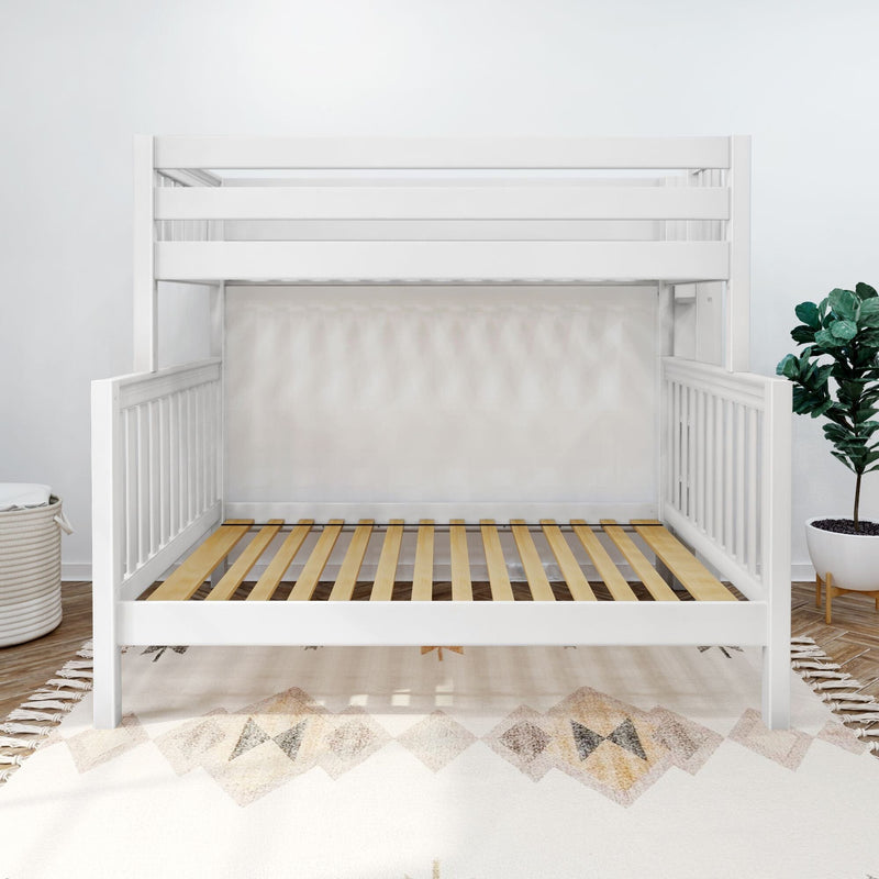 White wooden crib frame with slatted mattress support in a modern minimalist nursery featuring a patterned rug and potted plant