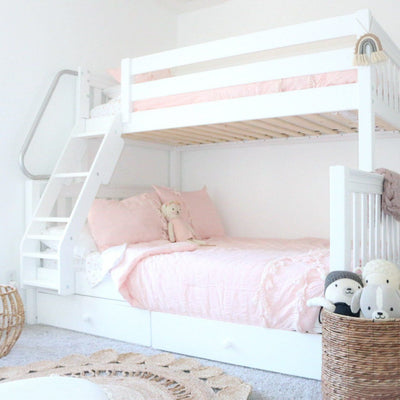 White wooden bunk bed with pink bedding, built-in storage drawers and woven basket of plush toys in a bright girls' nursery bedroom