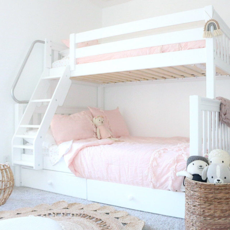 White wooden bunk bed with pink bedding, built-in storage drawers and woven basket of plush toys in a bright girls' nursery bedroom