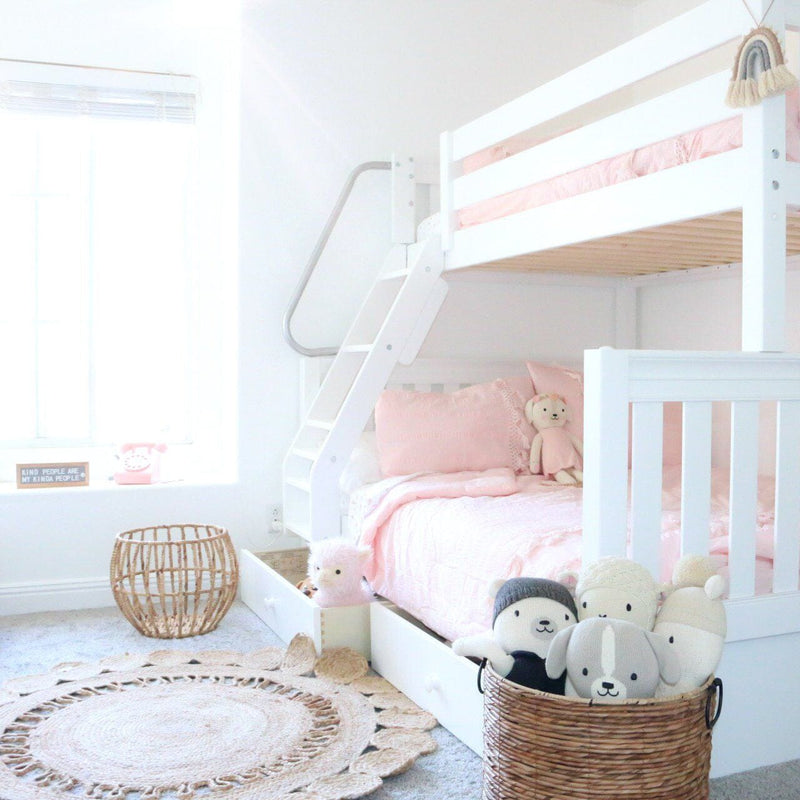 Sunlit children's bedroom with a white bunk bed and pink bedding, stuffed animals in a wicker basket, woven jute round rug and modern boho kids' bedroom decor