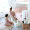 Two young girls in tulle dresses playing by a white bunk bed with pink bedding and under-bed toy storage in a pastel kids' bedroom