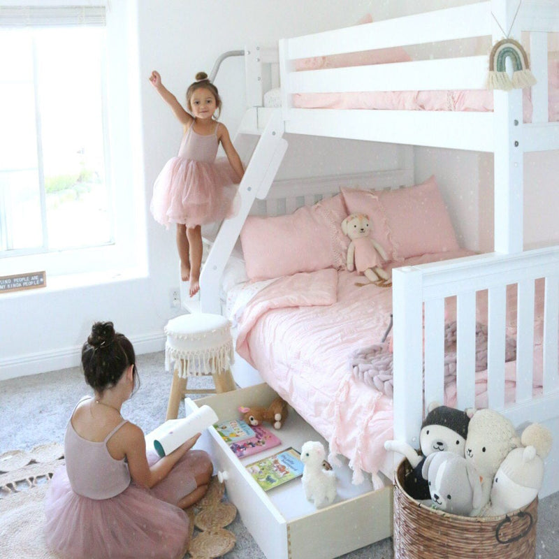 Bright pink girls' bedroom with white bunk bed, ruffled pink bedding, stuffed animals, under-bed book drawer and two girls in tutus reading