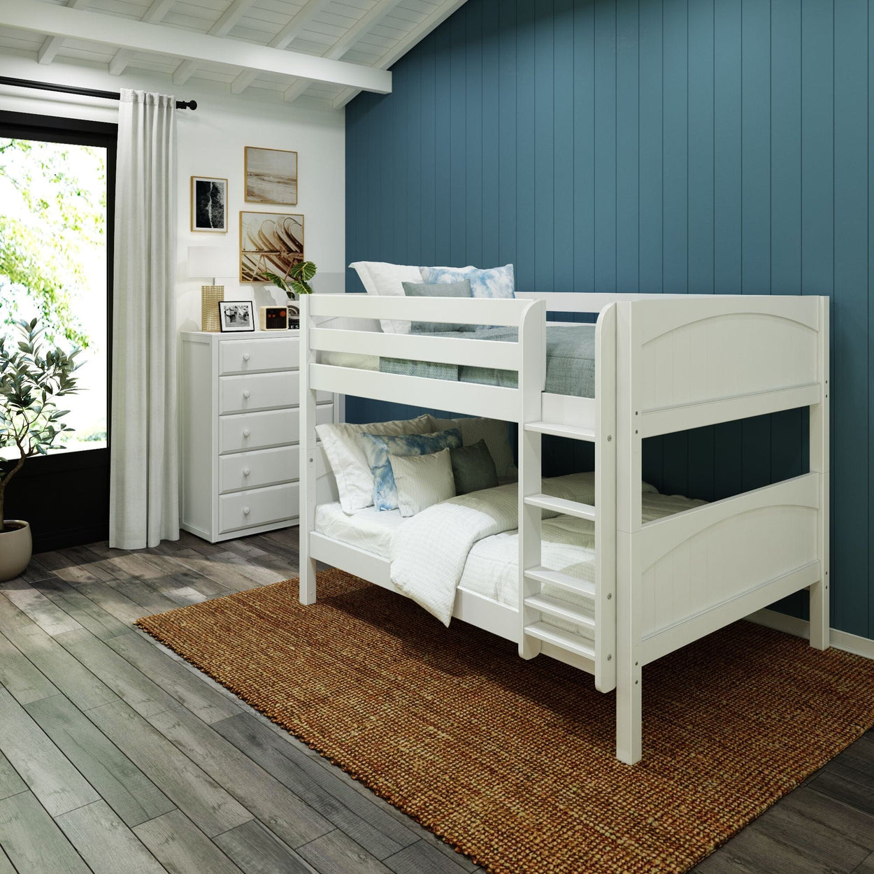 White wooden twin-over-twin bunk bed with ladder in cozy kids bedroom with blue accent wall, white dresser, woven rug, and natural light