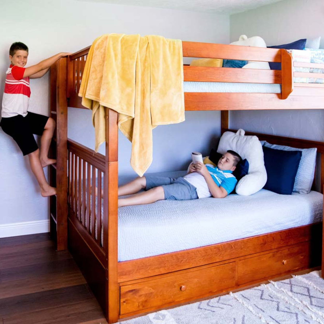 Children enjoying a wooden bunk bed setup, one climbing the ladder and the other reading on the bottom bunk.