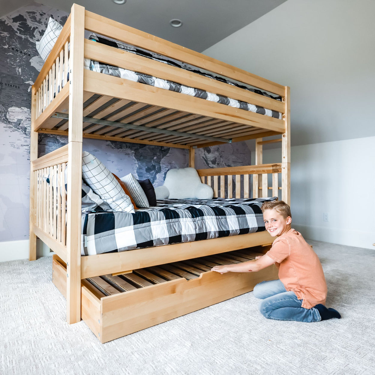 Boy smiling beside wooden bunk bed with pull-out storage drawer in modern bedroom.