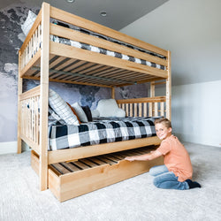 Boy smiling beside wooden bunk bed with pull-out storage drawer in modern bedroom.