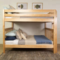 Solid wood twin-over-full bunk bed in natural finish with neutral linens, blue throw blanket, decorative pillows and geometric framed wall art — space-saving farmhouse bedroom furniture