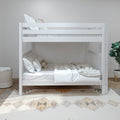 White modern twin-over-twin bunk bed with safety rails, neutral beige bedding and pillows in a minimalist kids' bedroom — space-saving children's room decor with rug and potted plant