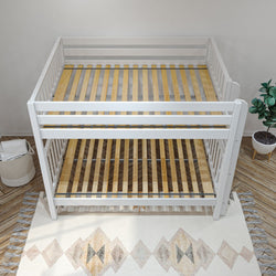 White wooden convertible crib-to-bunk bed frame with slatted pine mattress support in neutral nursery with rug and potted plant