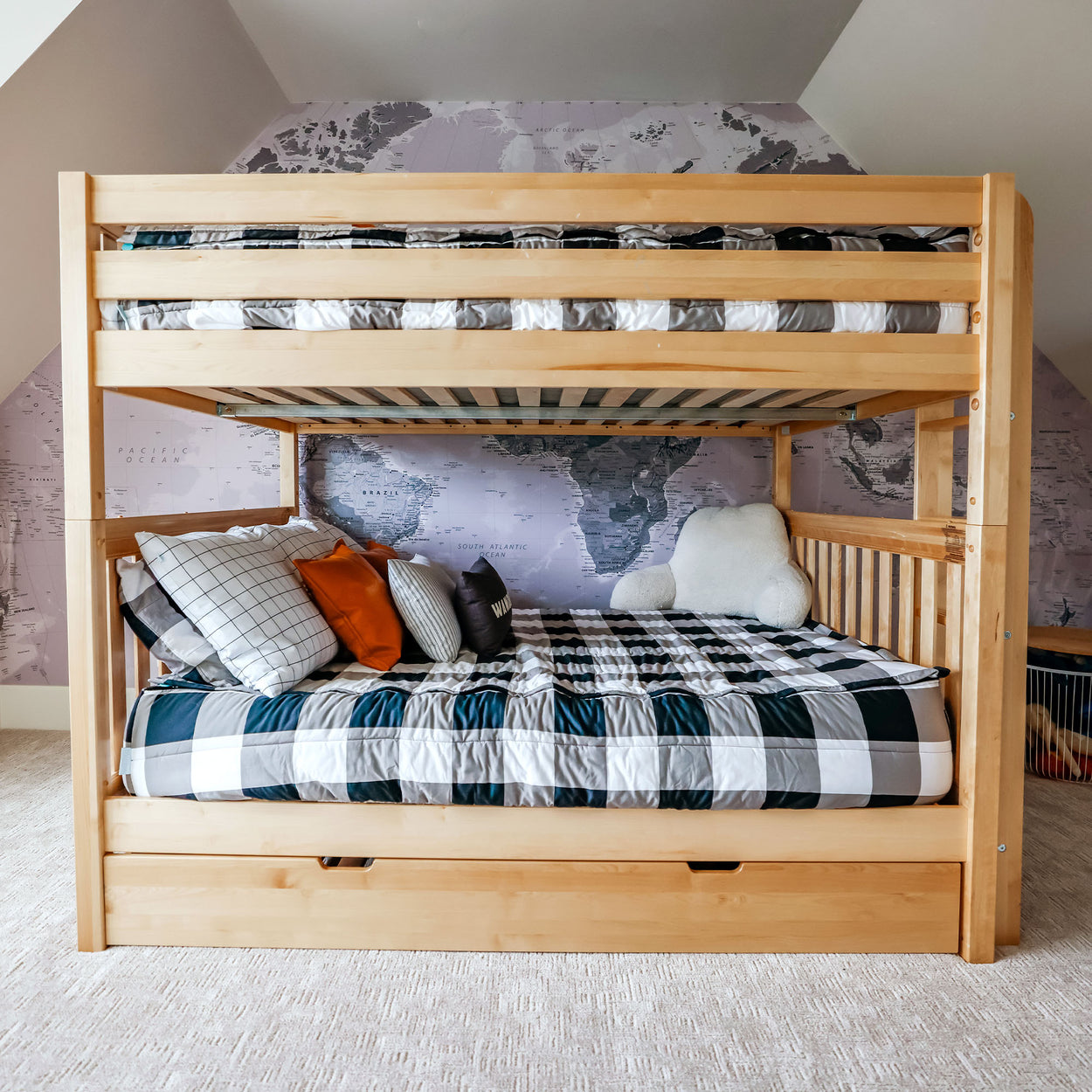 Wooden bunk bed with world map wallpaper and decorative pillows in a kid's bedroom.
