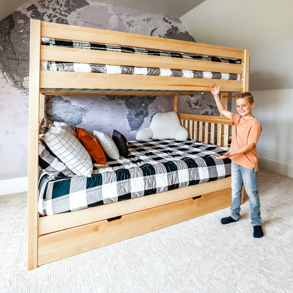 Boy proudly presenting a stylish wooden bunk bed in a modern bedroom with world map wallpaper.