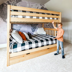 Boy proudly presenting a stylish wooden bunk bed in a modern bedroom with world map wallpaper.