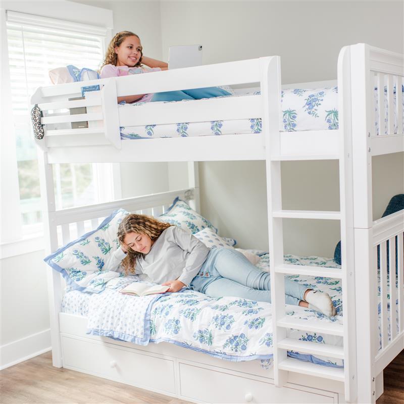 Two children on a white bunk bed with floral bedding in a bright room.