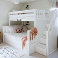 White wooden bunk bed with built-in storage stairs in a cozy kids bedroom with pastel throw, decorative pillows and hopscotch rug