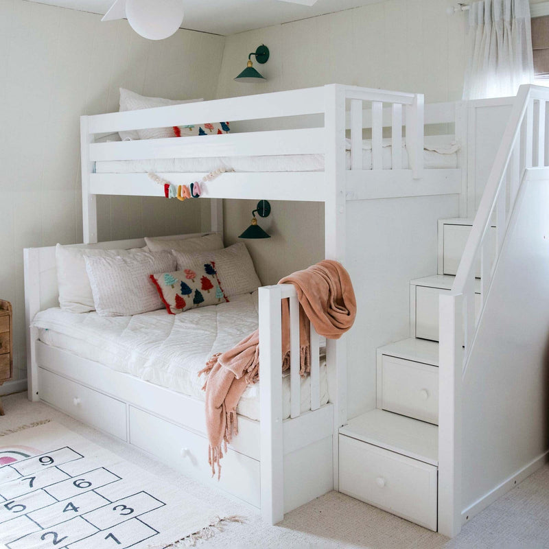 White wooden bunk bed with built-in storage stairs in a cozy kids bedroom with pastel throw, decorative pillows and hopscotch rug