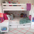 White bunk bed with under-bed storage in girls kids bedroom, cozy lower bed with colorful pillows, teal faux fur throw, donut plush, pink lamp and patterned rug