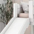 White wooden indoor slide attached to kids bed with soft pink mattress, gray pillow and leafy wall decor