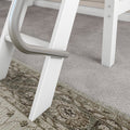Close-up of a white wooden A-frame ladder with a curved brushed-metal handrail and visible screws on textured beige-gray carpet in a home interior
