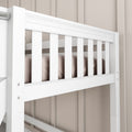 Close-up of white baby crib railing with vertical slats, beige bedding and paneled nursery wall