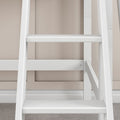 Close-up of a white wooden leaning ladder shelf with horizontal rungs against a beige wall on a carpeted floor, modern home decor