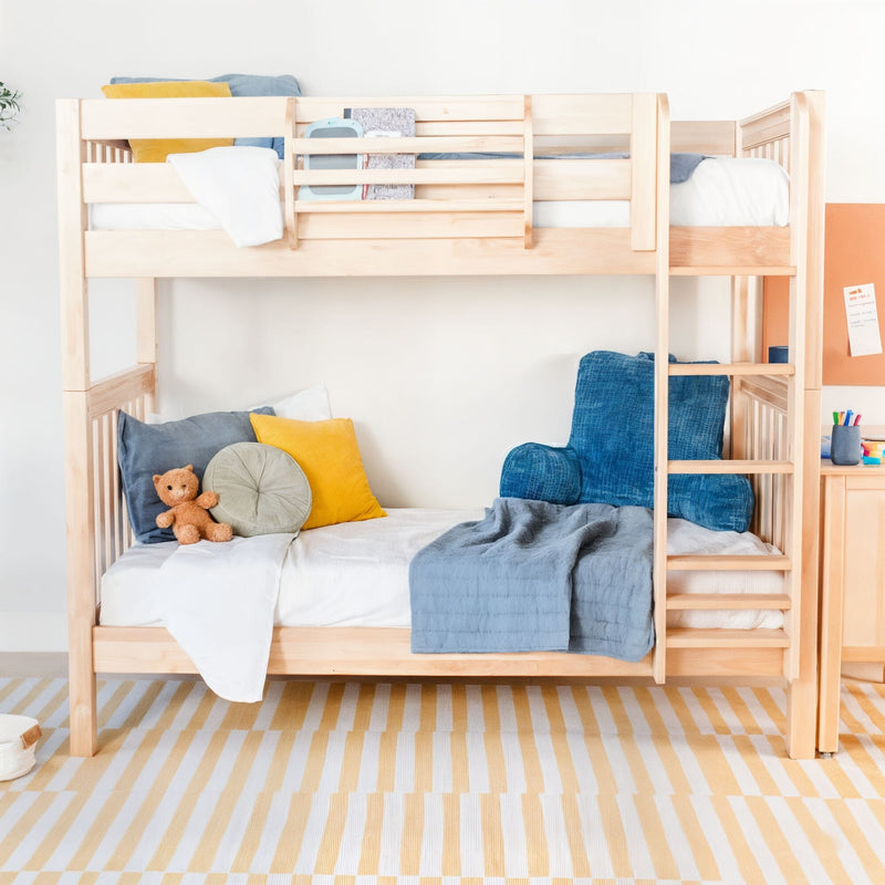 Light wood bunk bed in modern children's bedroom with blue armchair, yellow pillows, teddy bear and striped rug