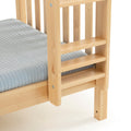 Natural wood bunk bed ladder and slatted guardrail with light blue striped mattress cover, close-up of light wood finish
