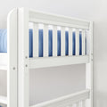 Close-up of white wooden crib railing with vertical slats and blue bedding, modern nursery baby crib guardrail and safety