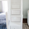 White built-in stair drawers integrated into bunk bed steps beside a blue quilt in a minimalist bedroom, showcasing space-saving under-stair storage and modern wooden furniture