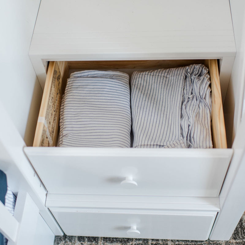 Neatly folded blue-and-white striped cotton sheets and pillowcases in an open white dresser drawer for organized linen storage