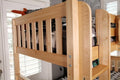 Natural maple twin-over-twin bunk bed with slatted safety rail and built-in ladder in a bright sunlit bedroom