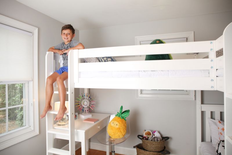 Kids white loft bed with ladder and study desk in a bright bedroom, smiling child on ladder, plush pineapple toy and basket of stuffed animals