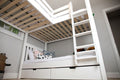 White wooden bunk bed with ladder and pull-out storage drawers in a modern children's bedroom with patterned pillows