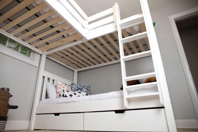 White wooden bunk bed with ladder and pull-out storage drawers in a modern children's bedroom with patterned pillows