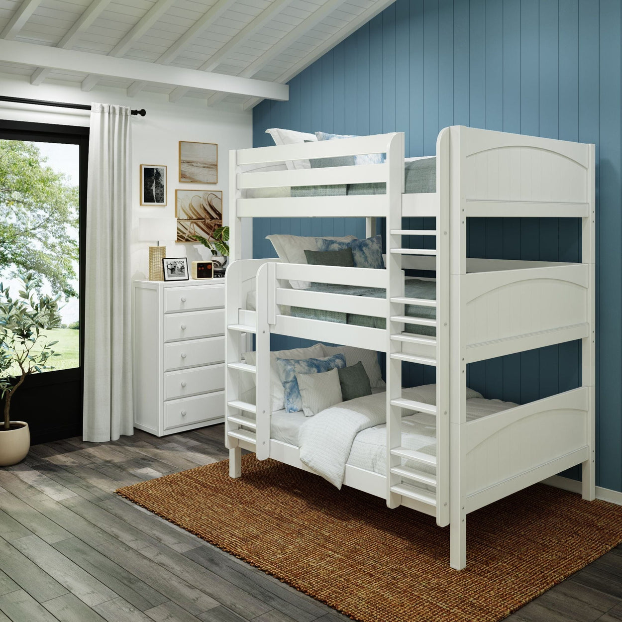 White wooden triple bunk bed in a modern kids' bedroom with blue shiplap wall, white dresser, jute rug and large window — space-saving design