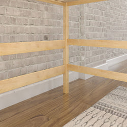 Simple wooden bed frame on hardwood floor with brick wall background.