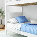 White wooden bunk bed with blue quilted bedding and star-pattern sheets in a bright children's bedroom, slatted upper frame, under-bed storage drawer and potted plant